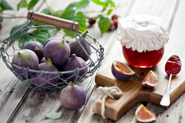 Fichi in un cesto accanto a un barattolo di marmellata su una tavola di legno