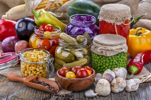 Canned cucumbers, onions, garlic and peas in a jar on a wooden table