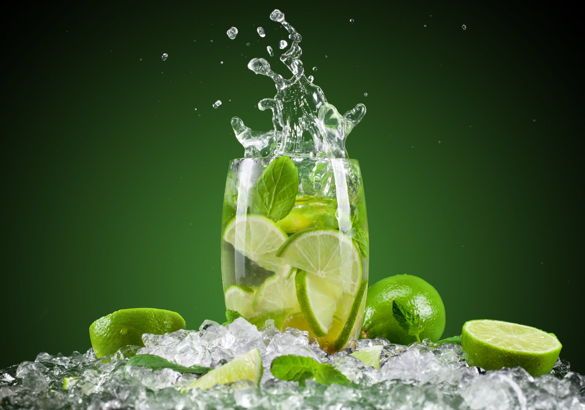 mojito cóctel copa de vino hielo lima cítricos fruta salpicaduras fondo verde