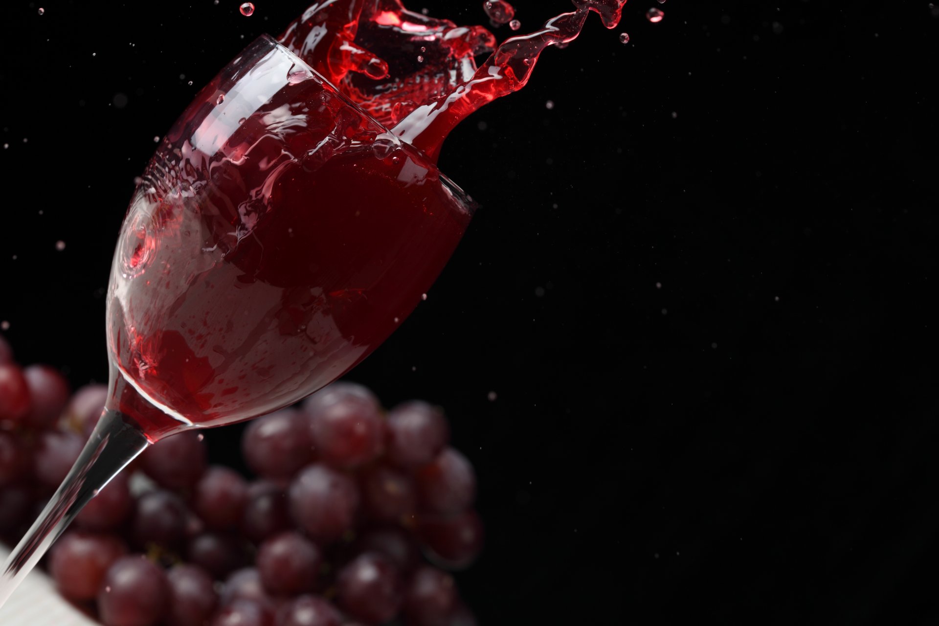 wein rot weinglas spritzer trauben schwarzer hintergrund