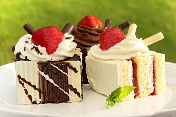 Iced cakes with jam decorated with chocolate tubes and strawberries on a white plate