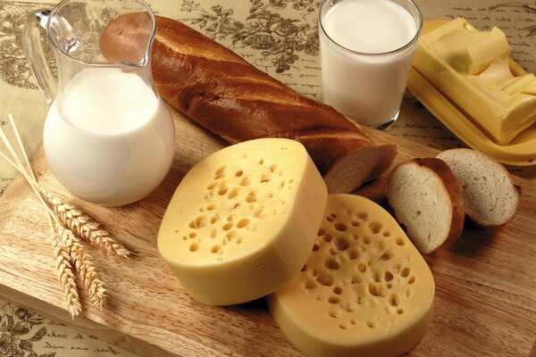 Essbares Stillleben aus Milch, Brot, Käse und Butter, garniert mit Getreide auf einem Holzbrett