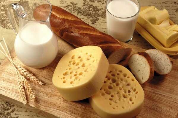 Съедобный натюрморт из молока, хлеба, сыра и масла, украшенный злаками на деревянной доске
