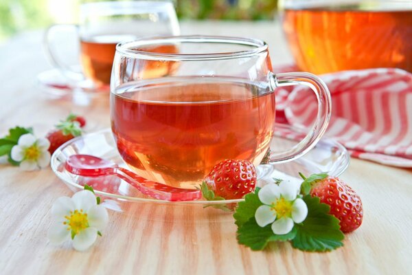 Una taza de té en la mesa con fresas en el fondo