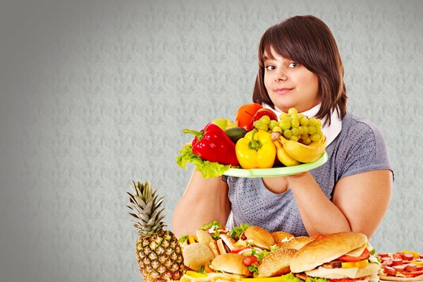 Das Mädchen hält ein Tablett mit Früchten. Auf dem Tisch liegen Burger und Sandwiches