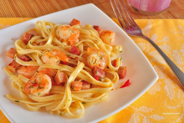 Tagliatelle deliziose con gamberi dorati in un piatto bianco come la neve