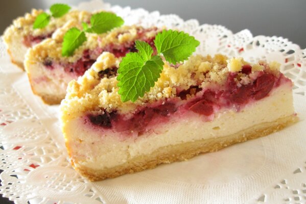 Pieces of cottage cheese and berry pie with mint leaves are on a napkin