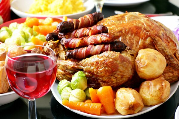 Fried chicken with a golden crust with baked vegetables and fried sausages on a plate. Nearby there is a glass of crimson wine