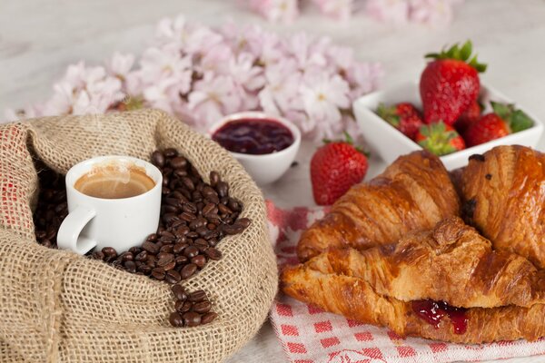 A cup of coffee among the beans and fresh croissants to it