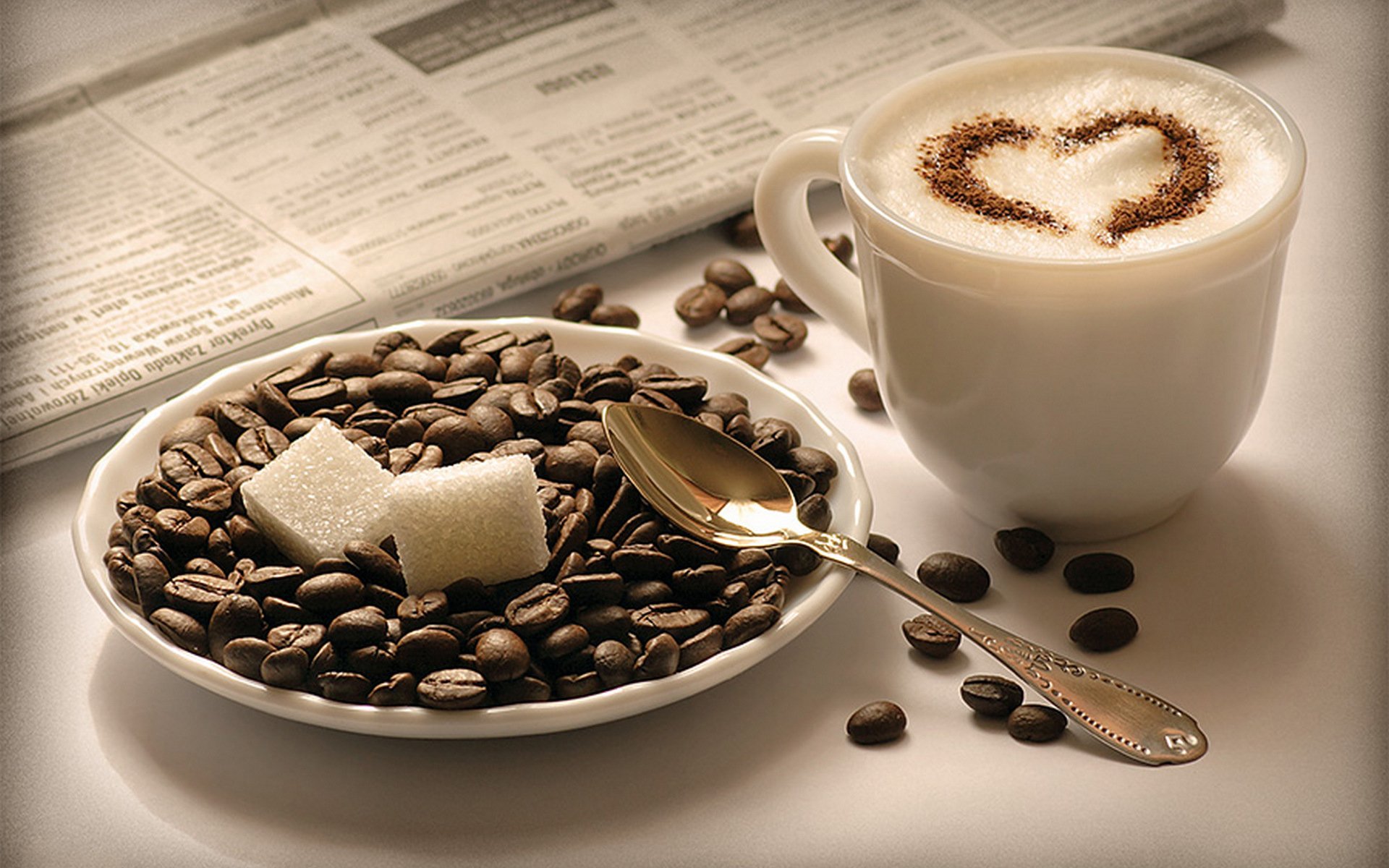 cappuccino filiżanka spodek kawa ziarna cukier kostki łyżka gazeta