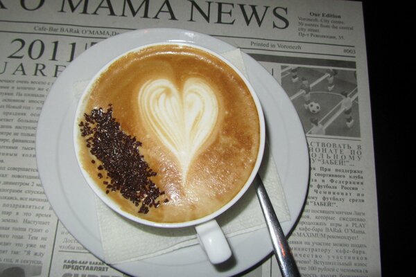Taza de café con espuma y cuchara en el periódico