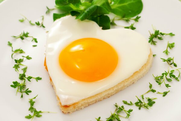 Fried egg on toast in the form of a heart with herbs on a plate