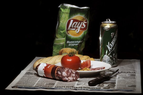 Patatas fritas, cerveza, tomate, pan y salchicha con un cuchillo en el periódico