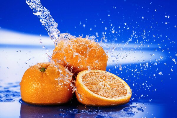 Juicy oranges in a splash of water on a blue background