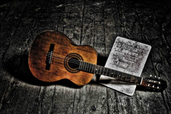 Guitar and sheet music lie on the wooden floor