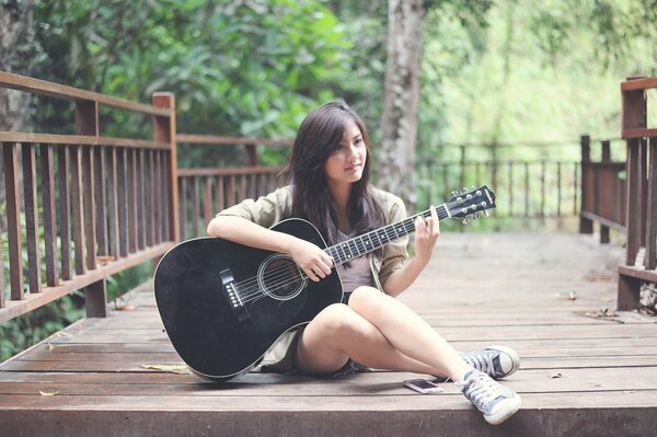 A girl with a guitar is sitting on a bridge