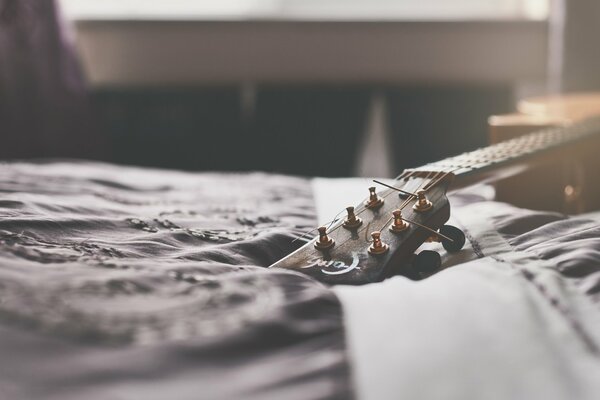 The neck of the guitar lying on the bed