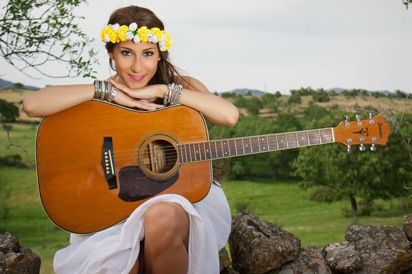 Schönes Mädchen in einem Kranz mit einer Gitarre