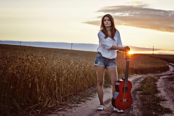 Chica con guitarra en el campo en el fondo de la puesta de sol