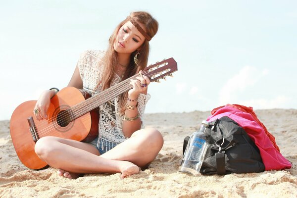 Ragazza ubriaca suona la chitarra seduta sulla sabbia