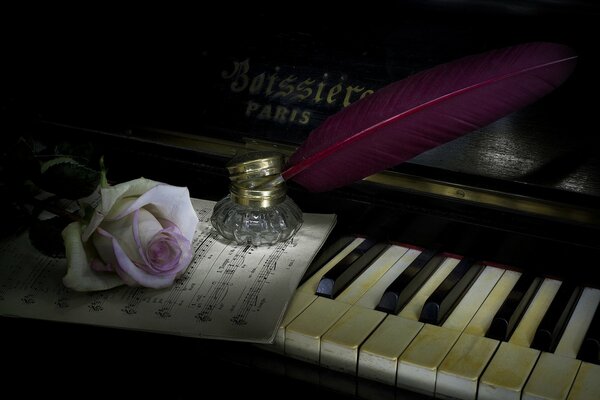 A rose with a feather is lying on the piano keyboard