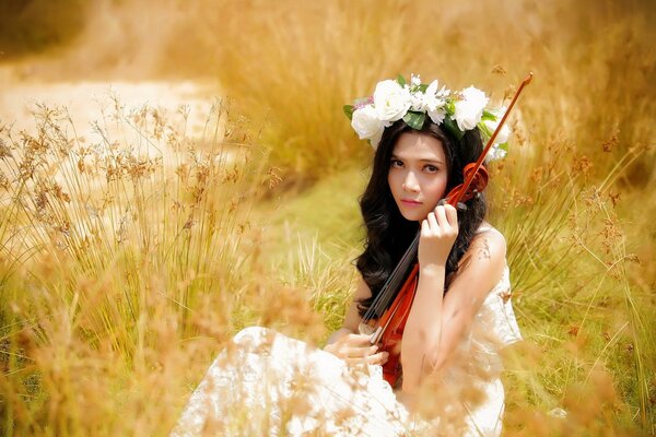 A girl in a wreath with a violin in the field