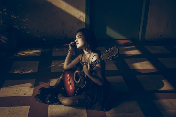 A girl with a guitar sitting on the floor