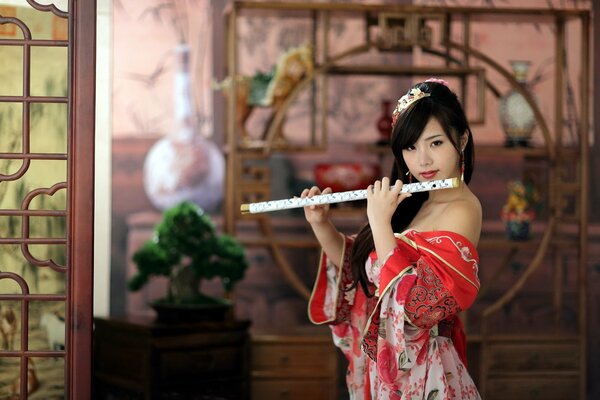 Chica asiática en vestido rojo tocando la flauta