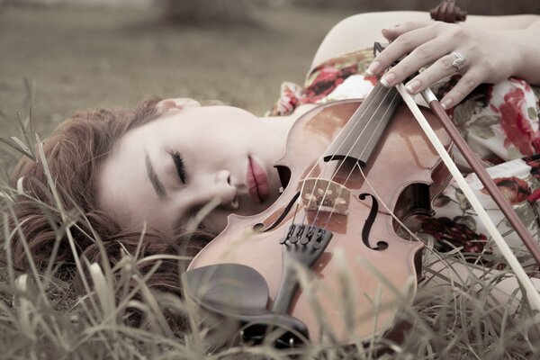 The girl is lying with a violin on the grass