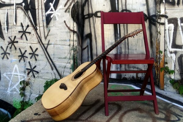 Guitar near a red chair with a painted wall