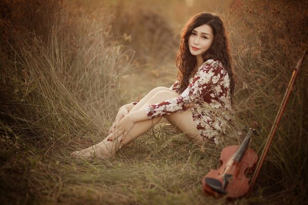 A girl in a dress with flowers is sitting next to a violin