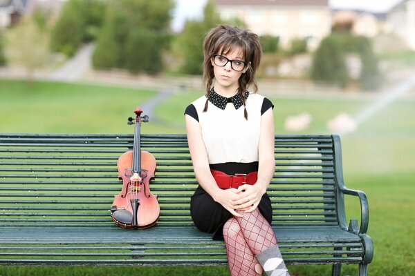 A girl with a violin is sitting on a bench