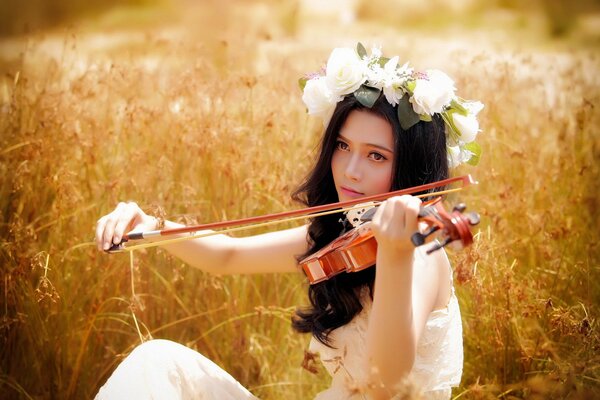 A girl in a wreath plays the violin in a field