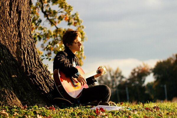 Trauriger Typ mit einer Gitarre unter einem Baum