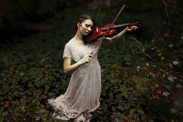 Una ragazza in un lungo abito bianco suona il violino