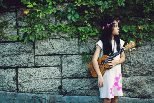 Красивая девочка в белом платье играет музыку на гитаре