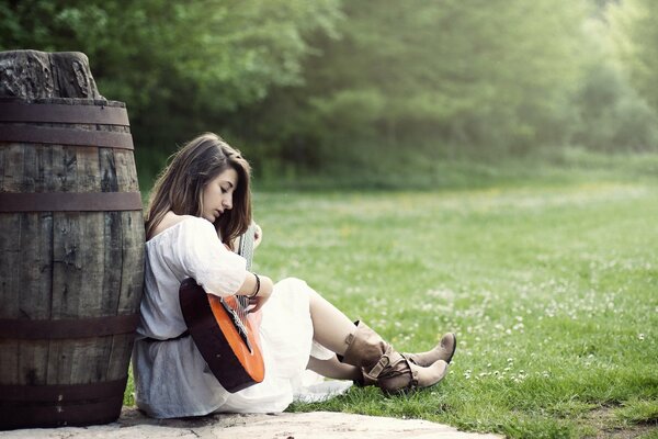 Das Mädchen mit der Gitarre sitzt in der Nähe des Fasses