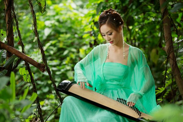 An Asian girl in a green dress plays a musical instrument