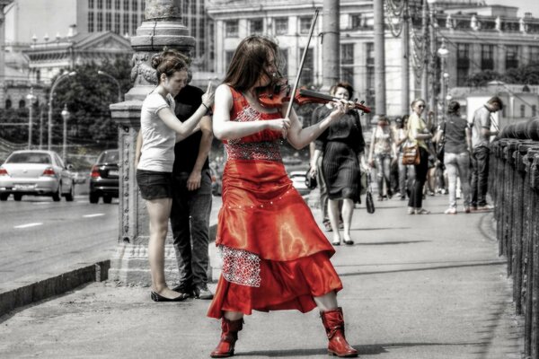 A girl in red plays a violin in the middle of the street