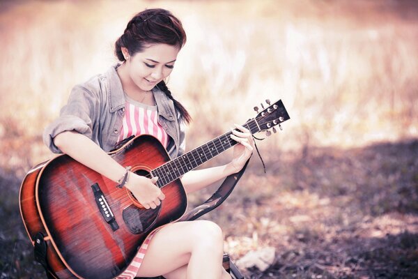 Chica tocando la guitarra, sentado en la naturaleza