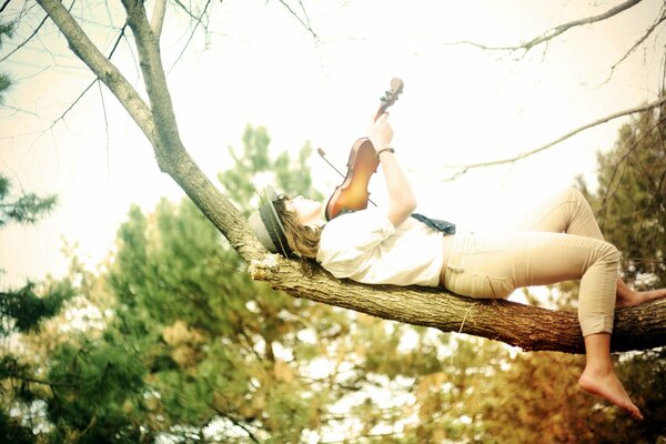 Una niña yace en un árbol con un violín en sus manos