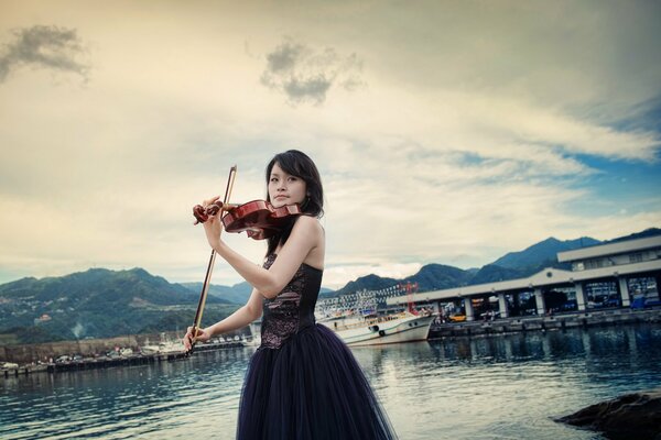 Violinist in evening dress on the shore of the bay