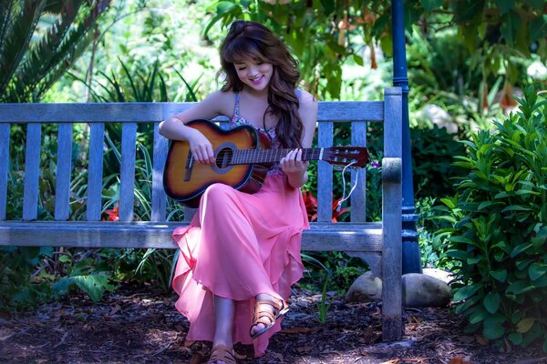 The brunette is sitting on a bench and playing the guitar