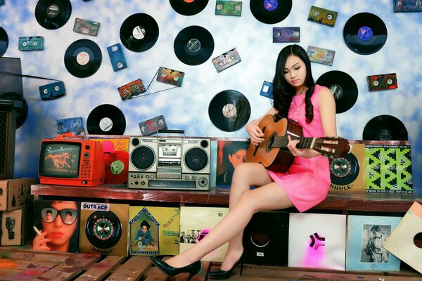 Девушка с гитарой сидит у стены с пластинками