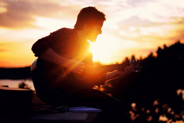 A guy playing guitar at sunset