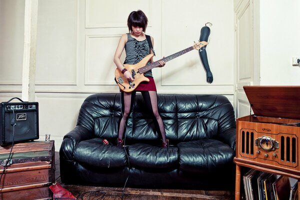 A girl plays an electric guitar standing on the couch