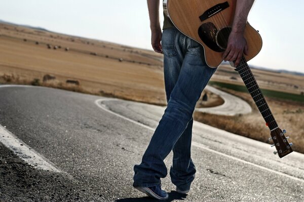 Un homme avec une guitare marche sur la route