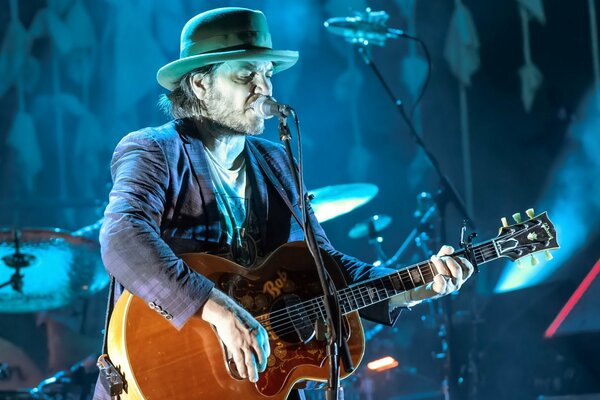 Músico con sombrero y guitarra cantando en concierto