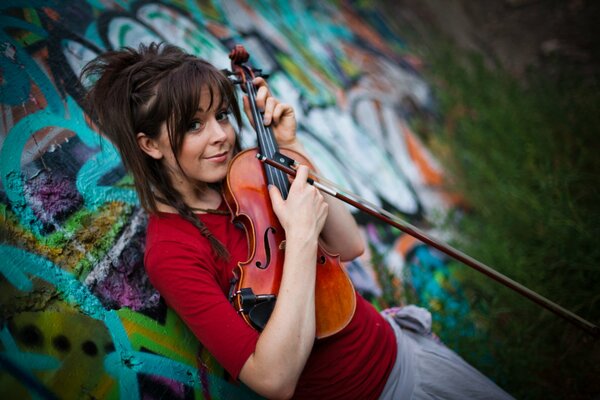 A beautiful girl in a red blouse holds a violin in her hands
