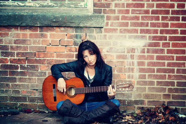 A girl with a guitar at a brick wall